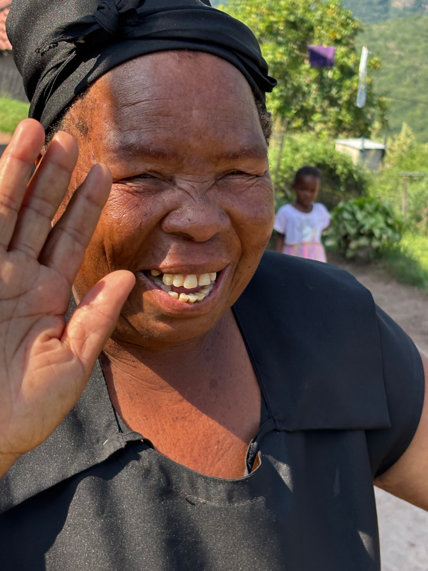 A gogo laughing and waving in front of her home on the hillside