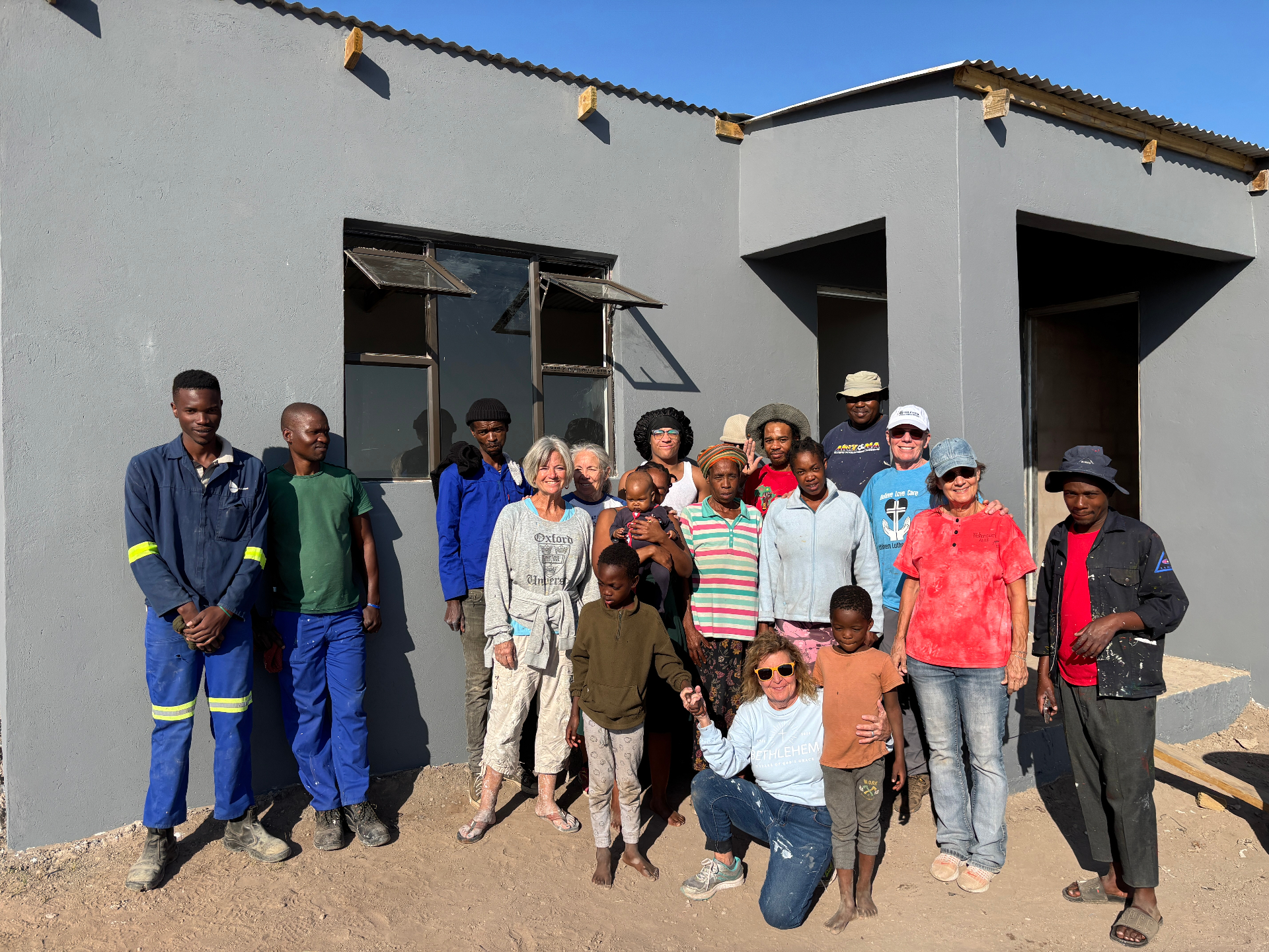 Gogo Ngcayi's family, neighbors, and the team gathered in front of the new secure home