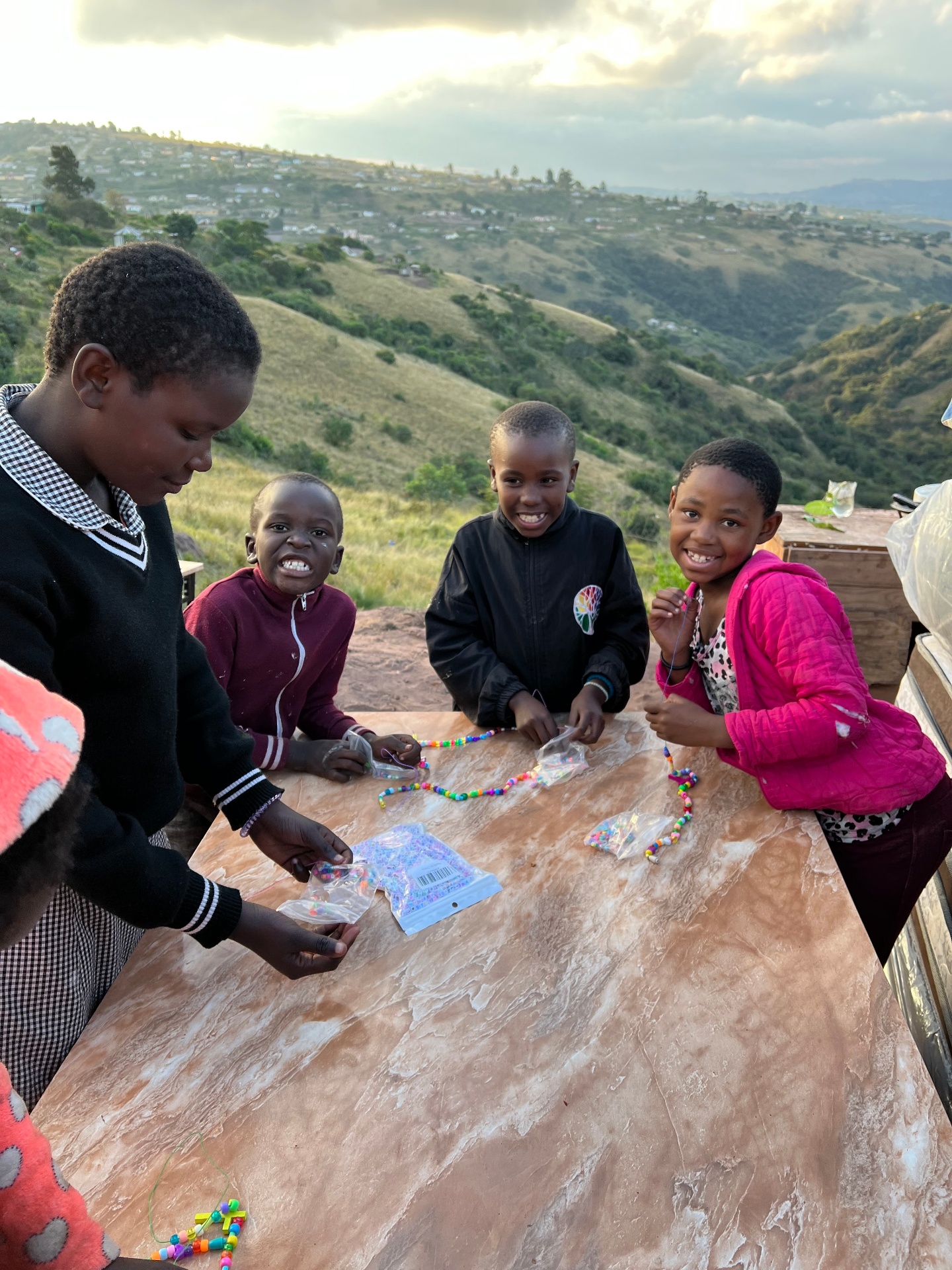 Children stringing beads on the hillside outside the home