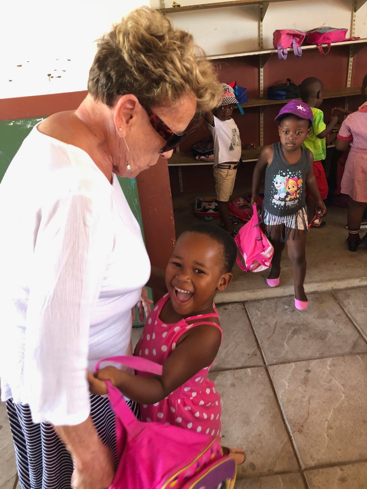 A laughing girl in a pink dress hugging a friend of the mission