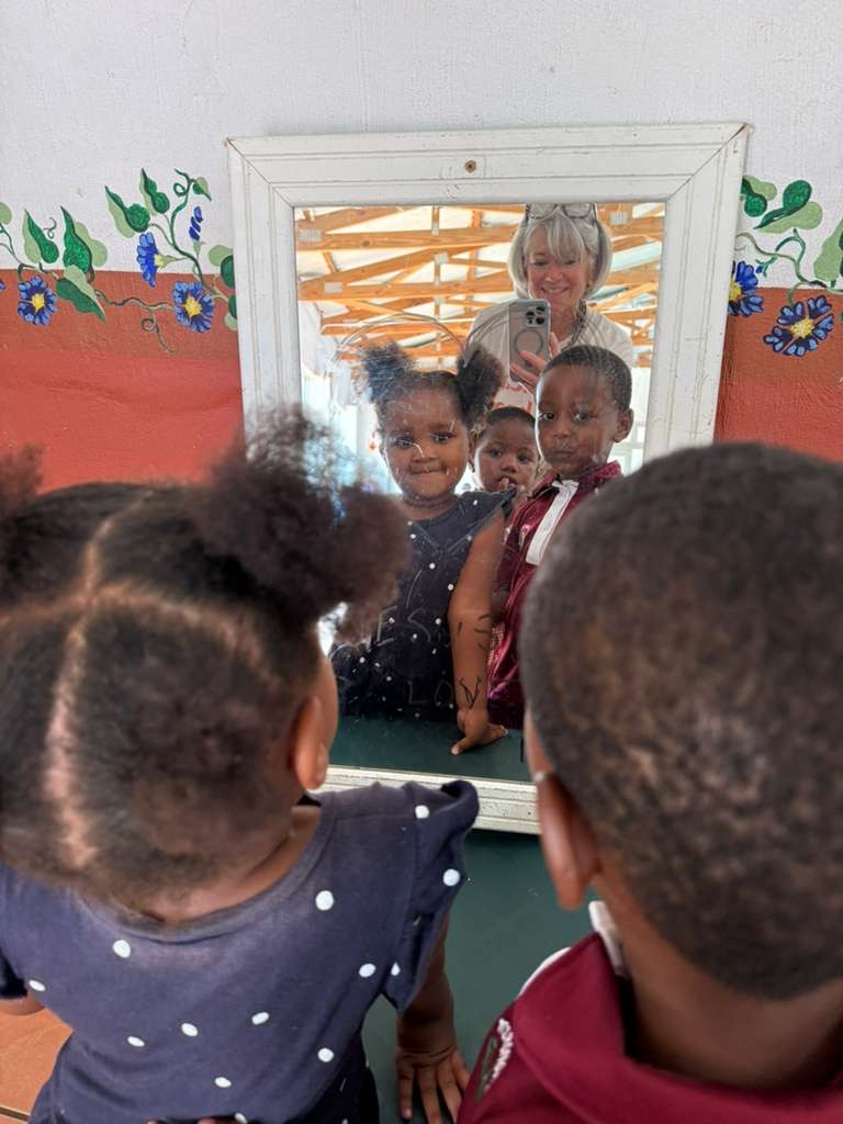 Three preschoolers laughing at their reflection in a classroom mirror