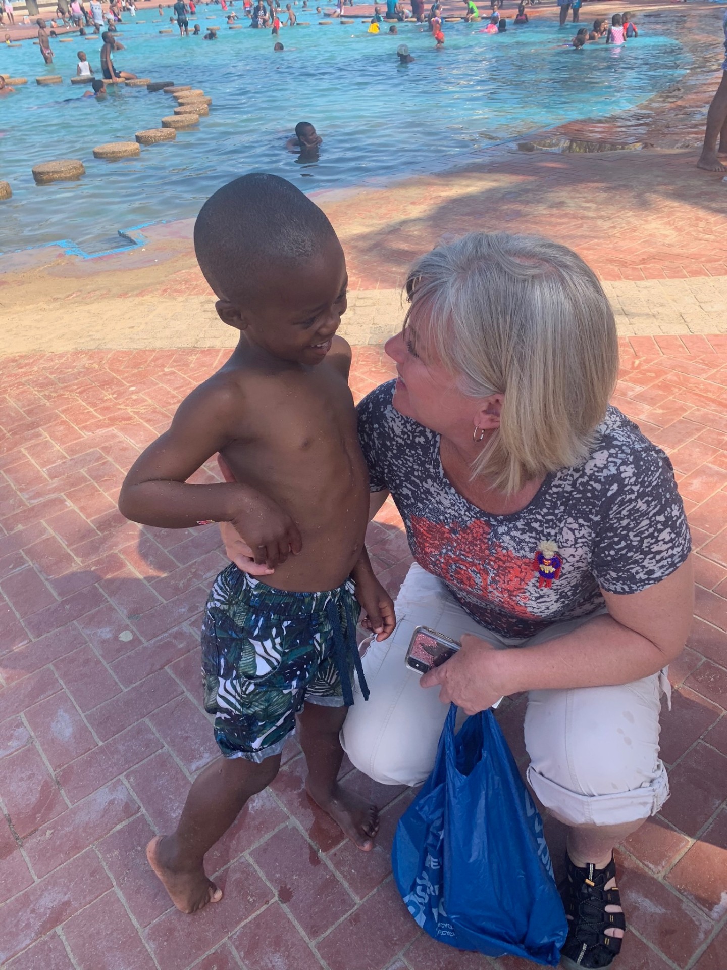A small boy laughing close to a kneeling friend beside the public pool