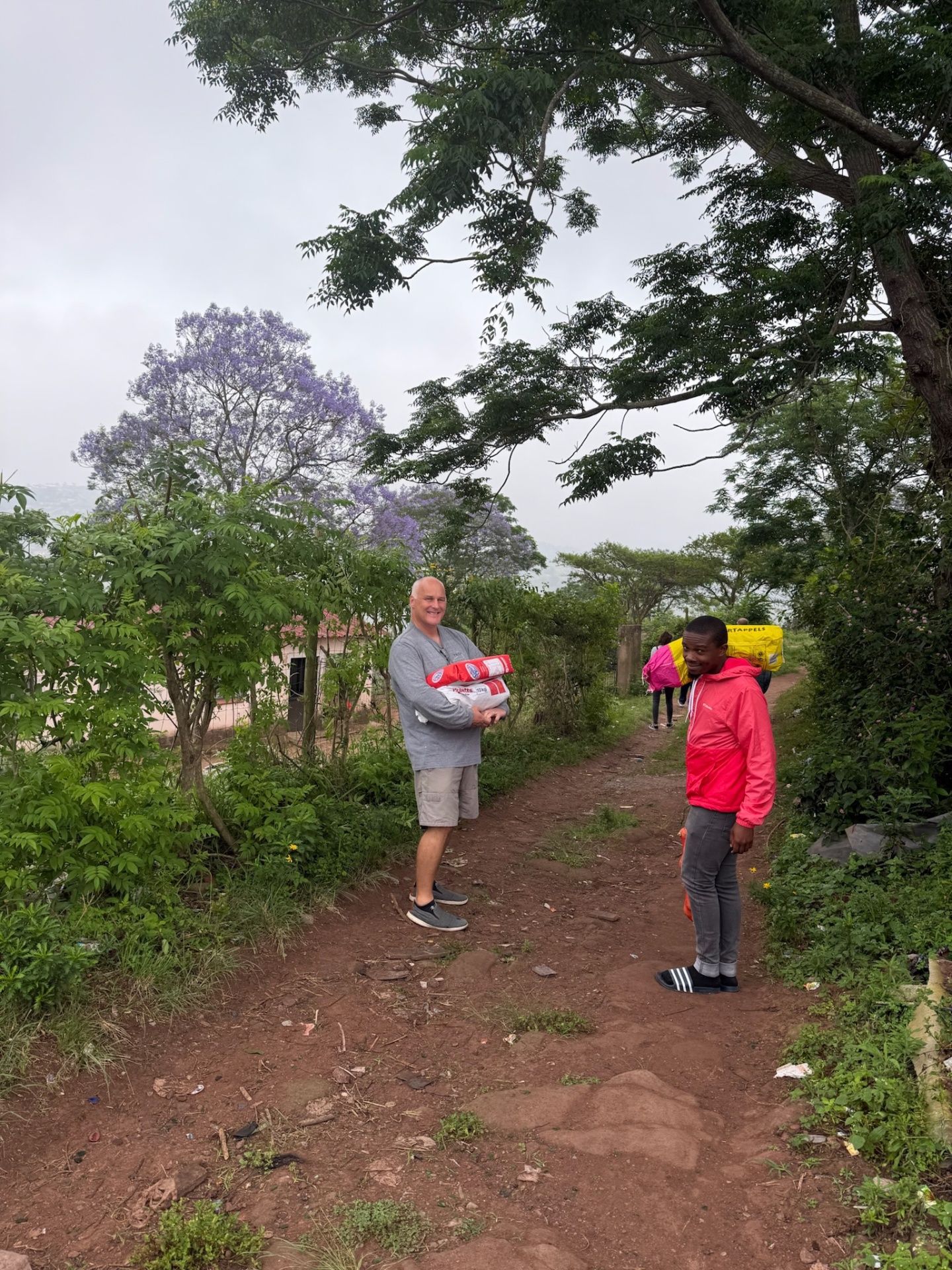 Delivering food parcels along a path in Ntshongweni, jacaranda in bloom