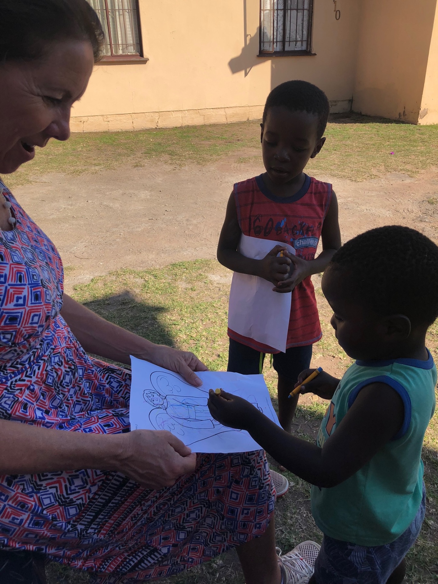 A mission friend coloring with two small boys outside