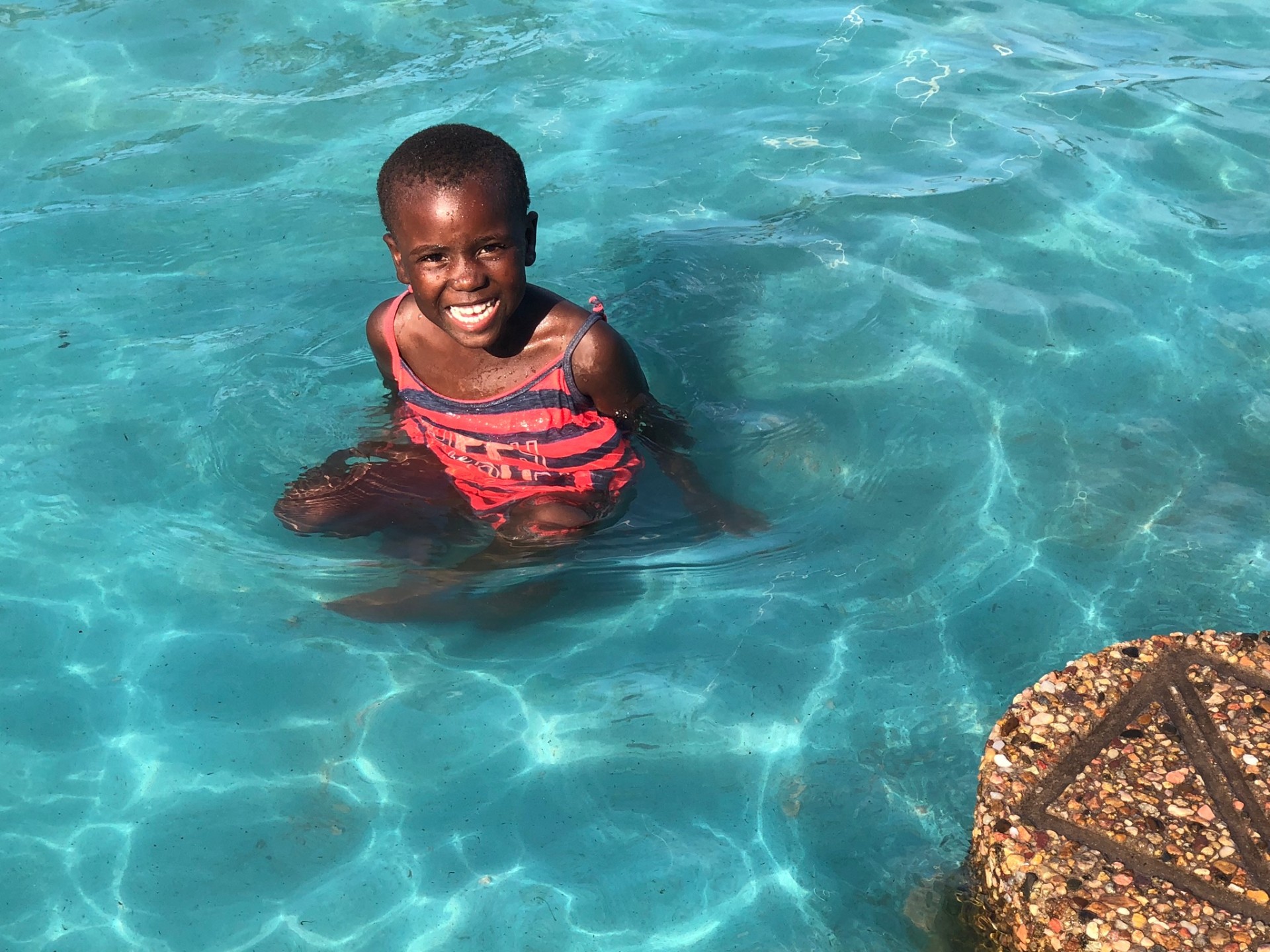 A young girl beaming in the bright blue pool
