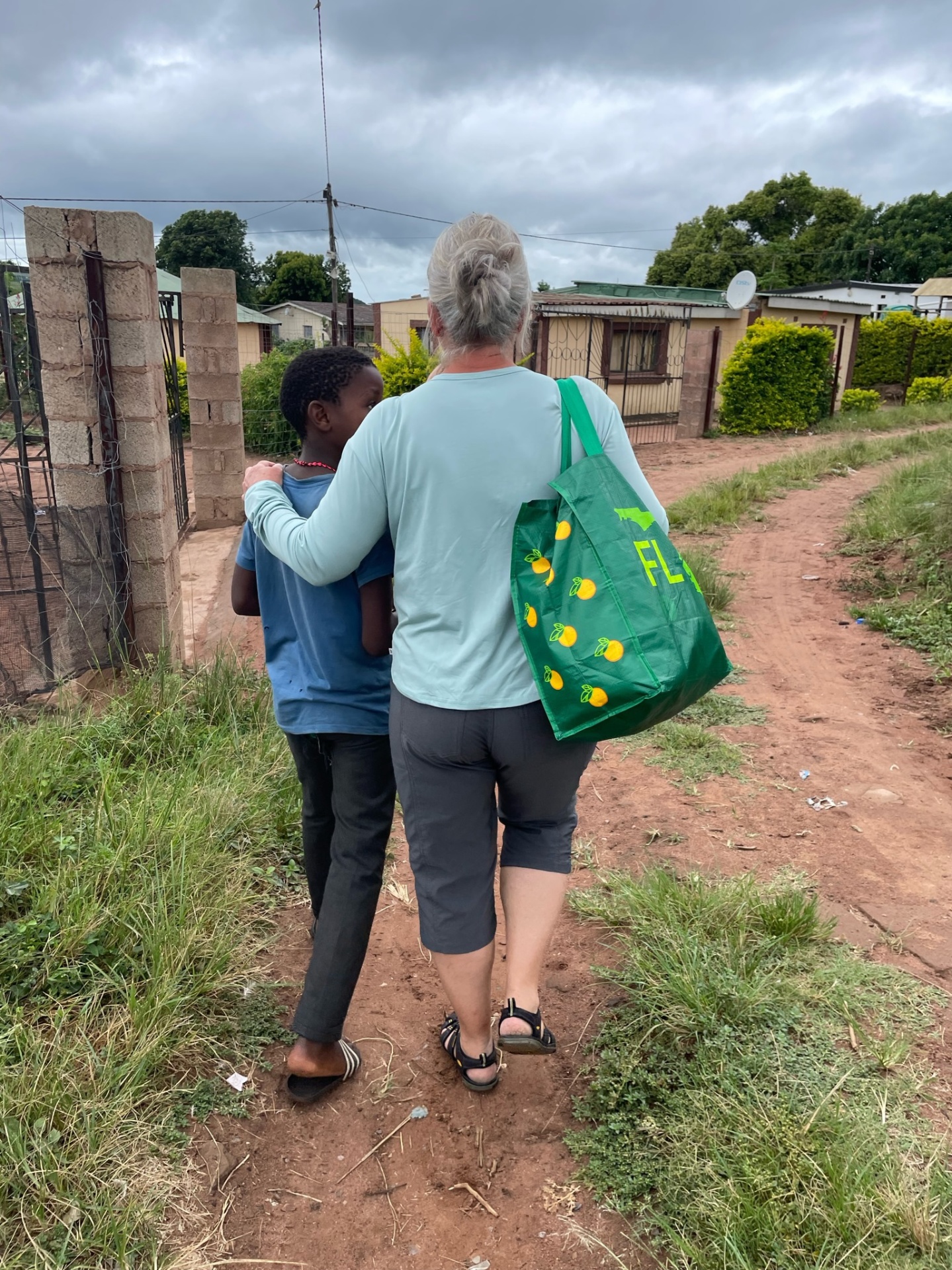 A friend walking arm in arm with a child on a dirt road in Ntshongweni
