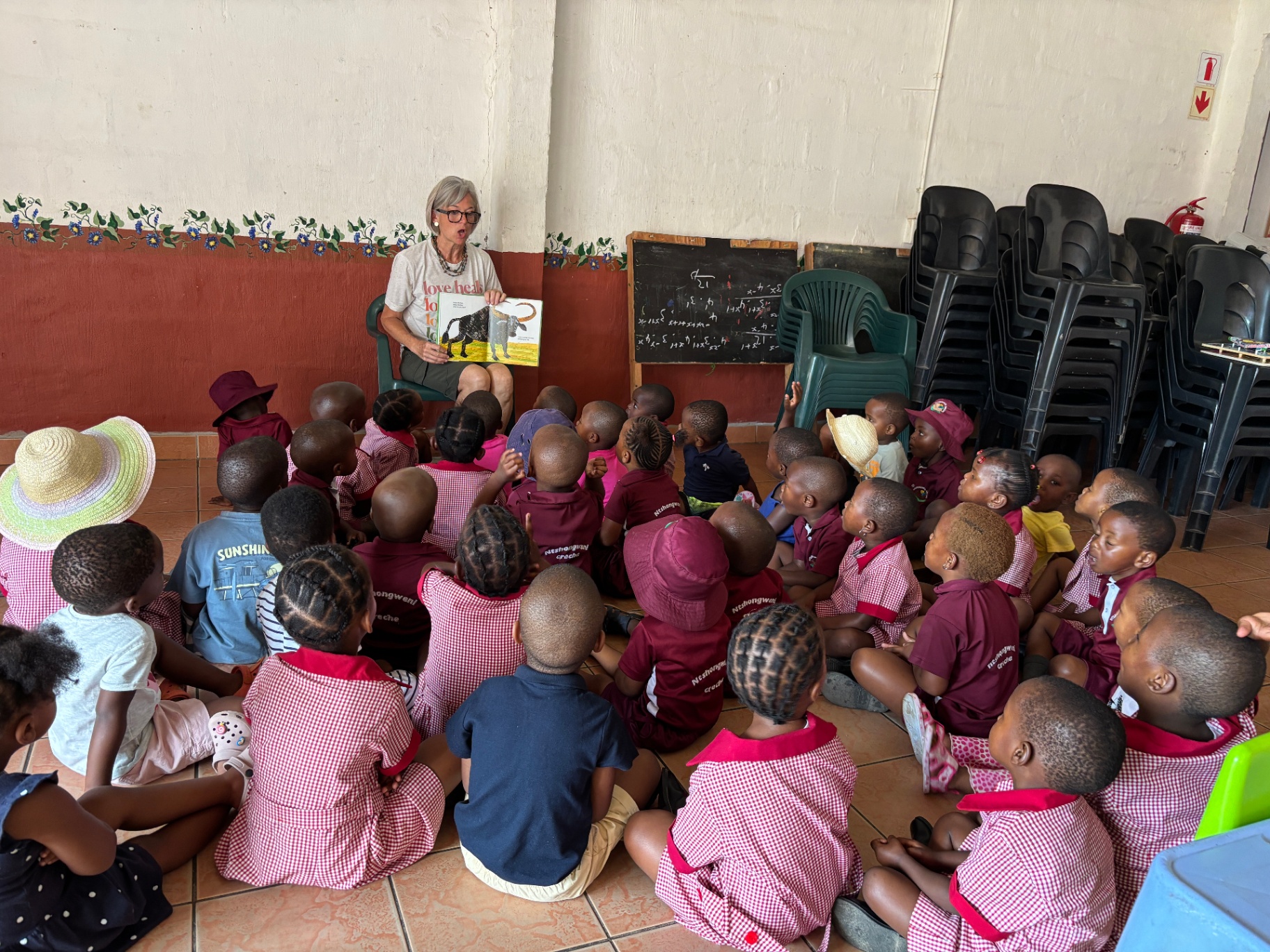 A volunteer reading a picture book to dozens of preschoolers seated on the creche floor
