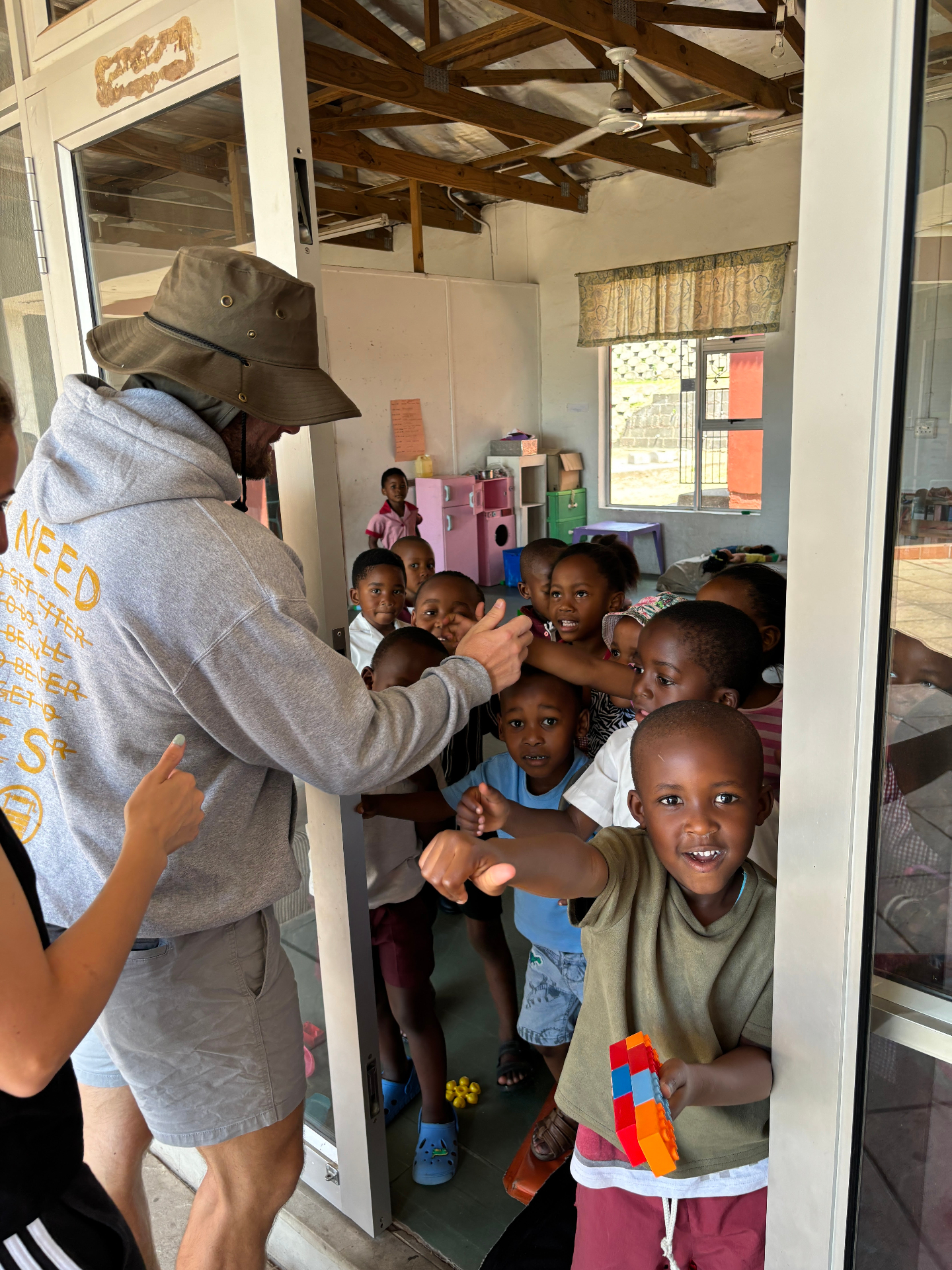 A member of the team giving thumbs up with a room full of children at the preschool