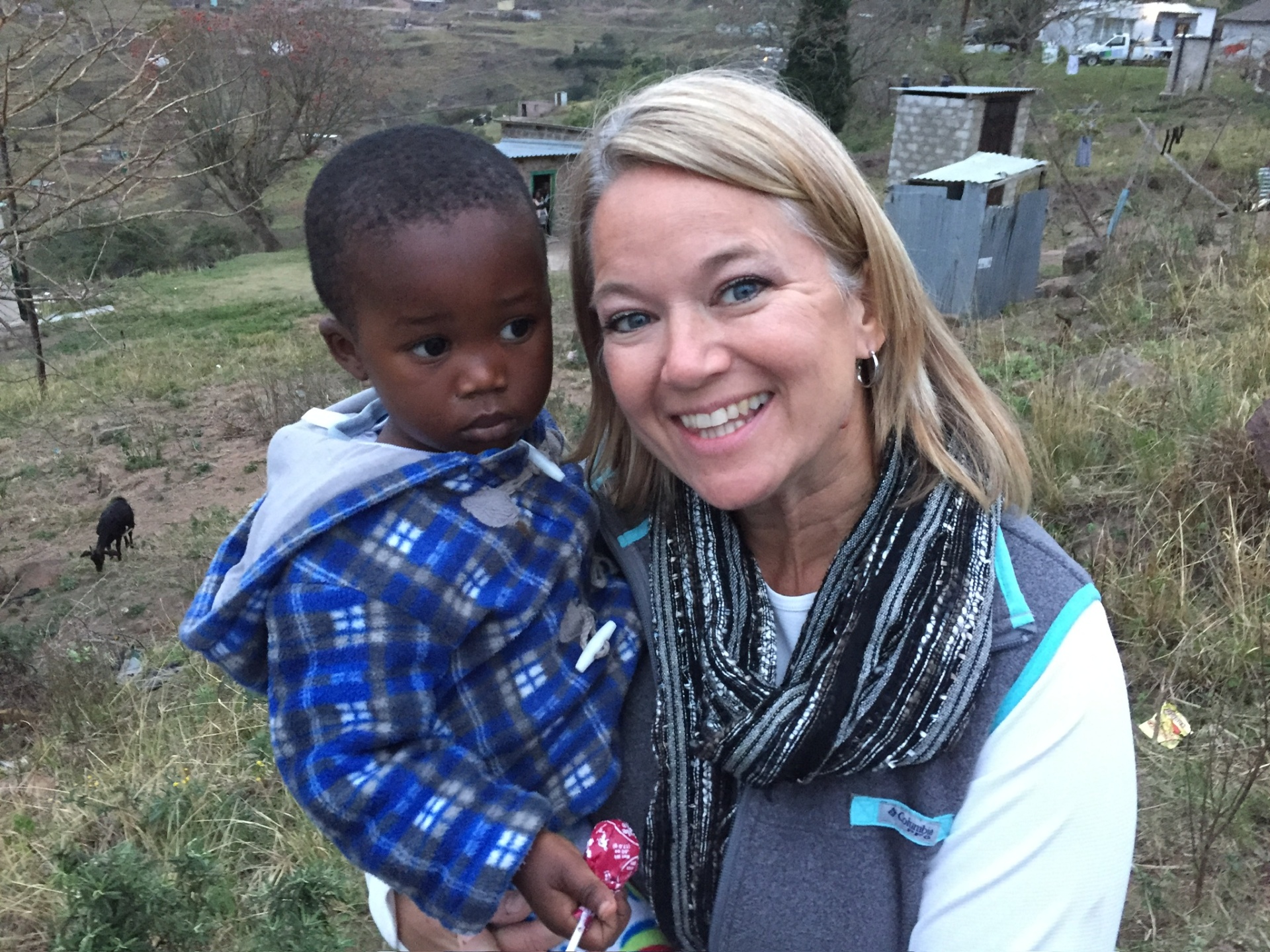 A friend holding a Ntshongweni toddler with the hillside behind them