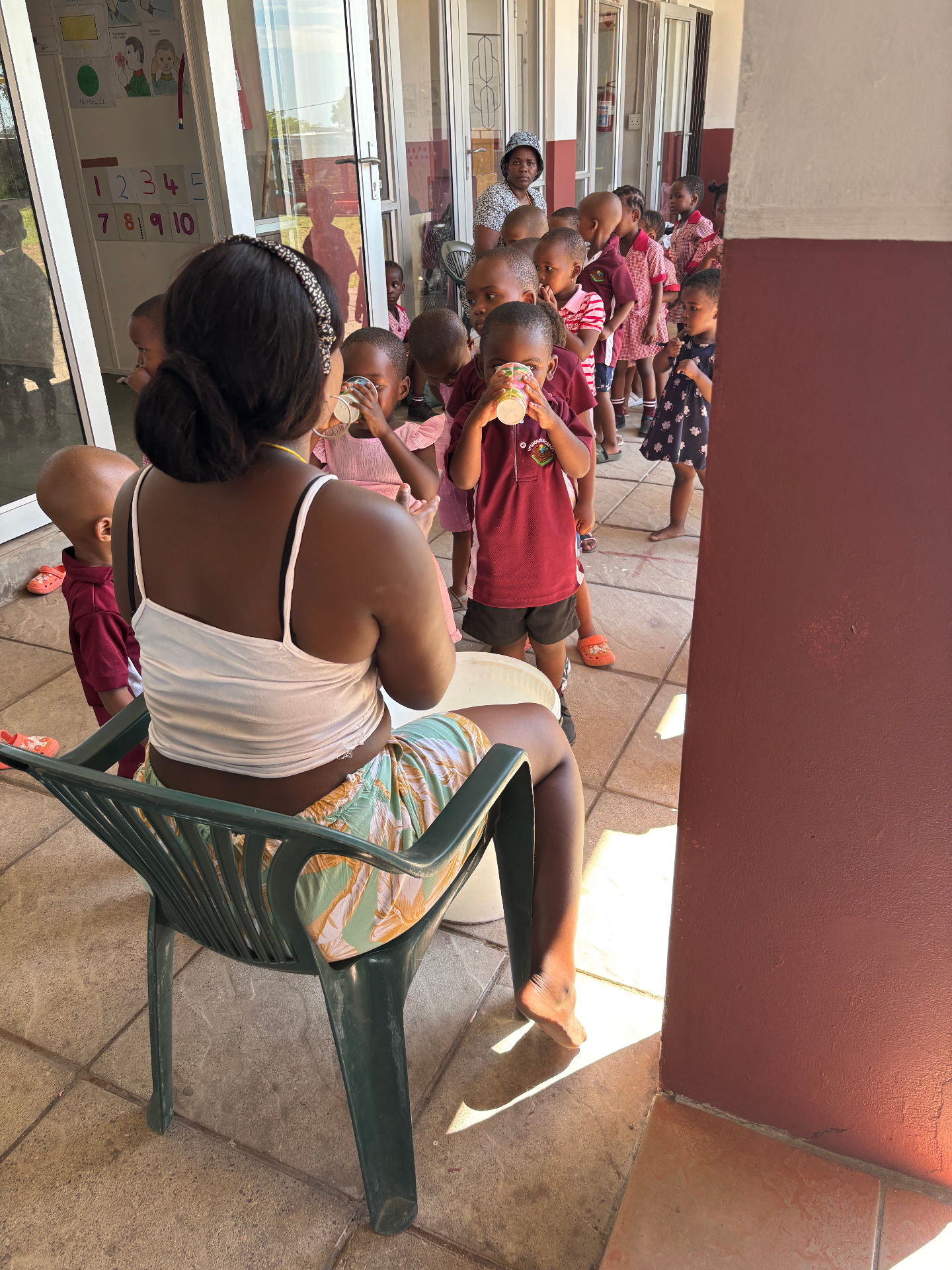 A teacher handing out snacks to a line of preschoolers on the creche porch