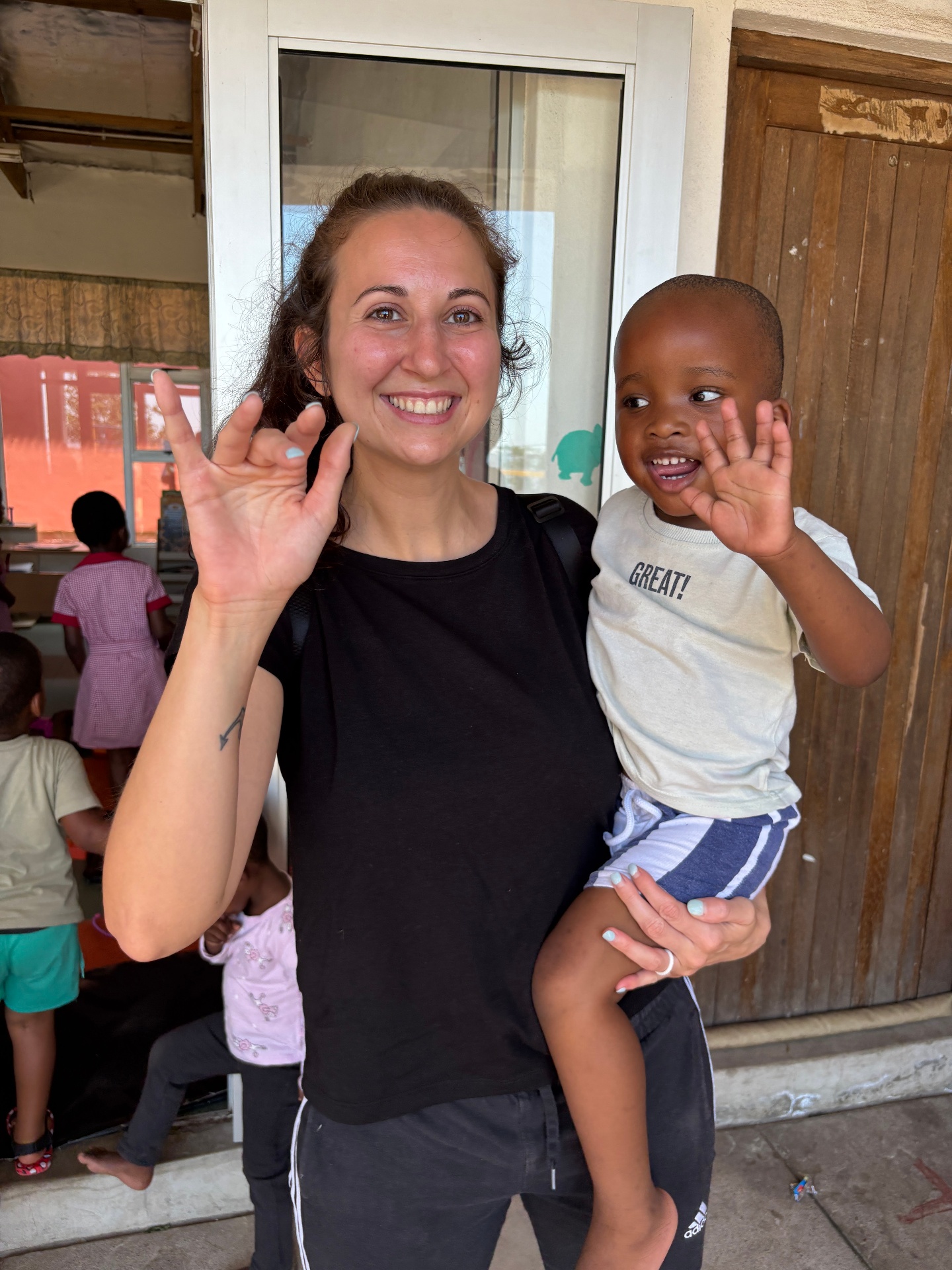 A visiting teacher holding a smiling preschooler as they wave together