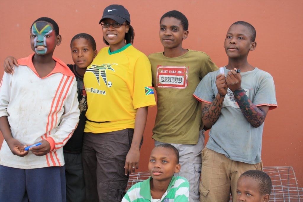 A young South African friend in a Bafana Bafana jersey standing with five Ntshongweni boys against an orange wall