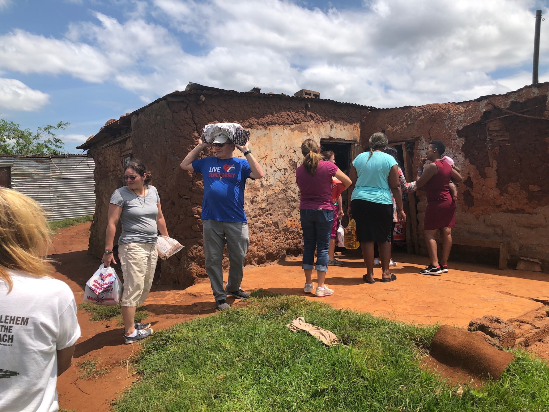 The team carrying packed food parcels past the wall of a Ntshongweni family home during a delivery