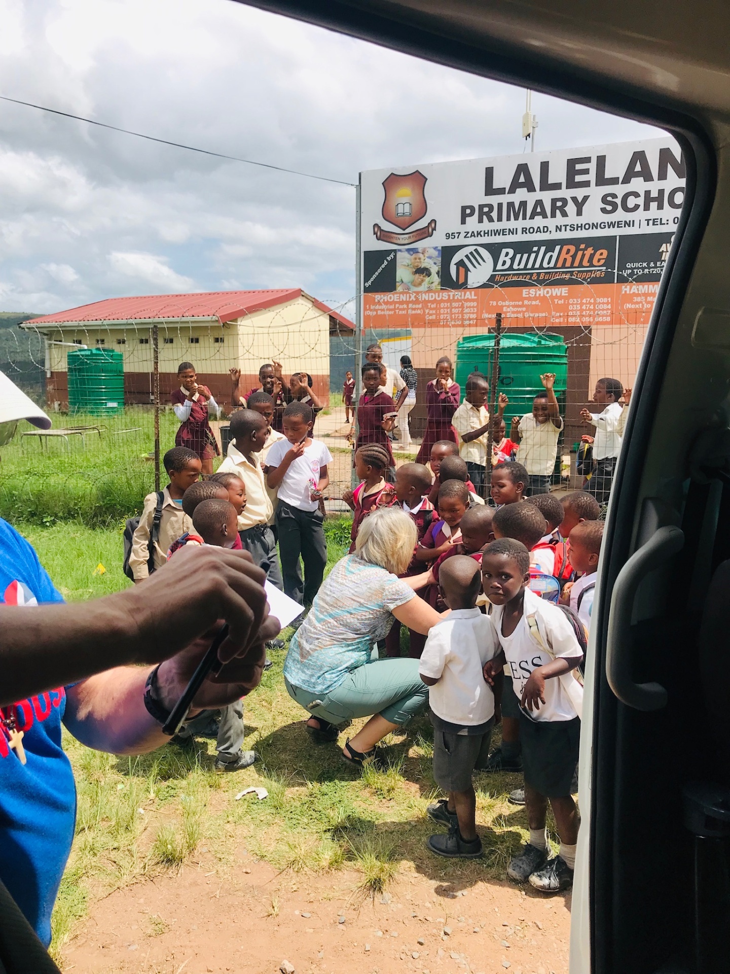 A long-time friend of the mission kneeling to greet Lalelani Primary School children