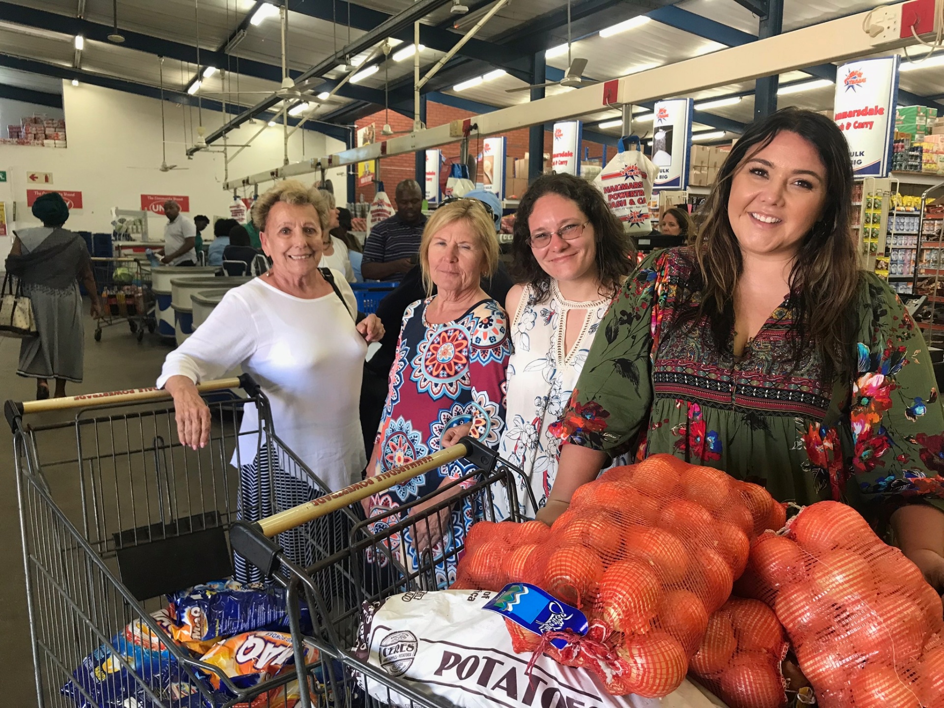 Four mission friends smiling with carts full of potatoes and staples while shopping for food-parcel supplies at the wholesaler