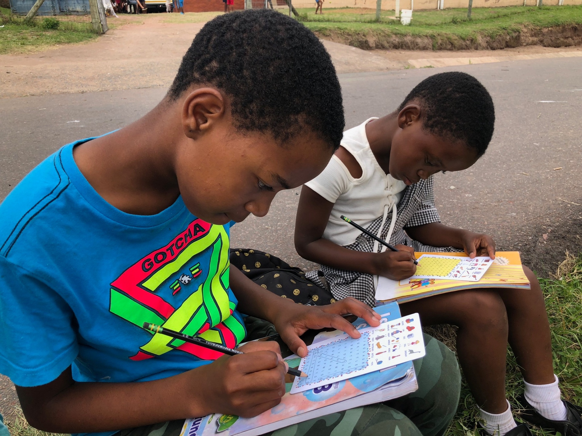 Children working through puzzle books on a roadside curb