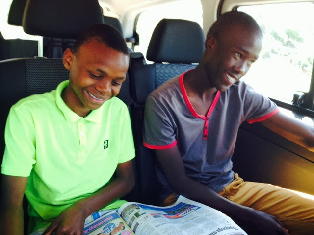 Two young men laughing over a newspaper in the van