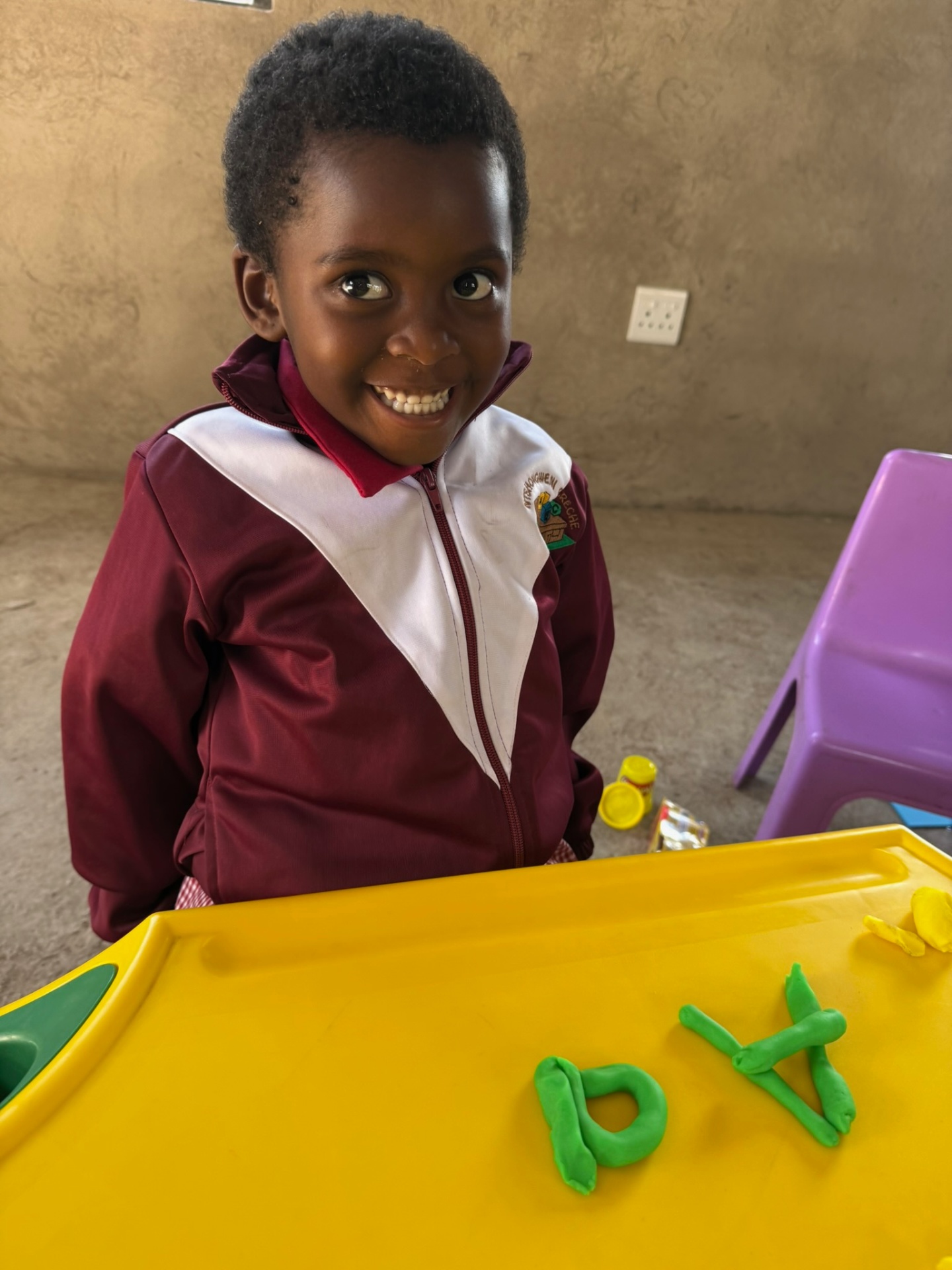 A crèche student smiling while forming play-dough letters