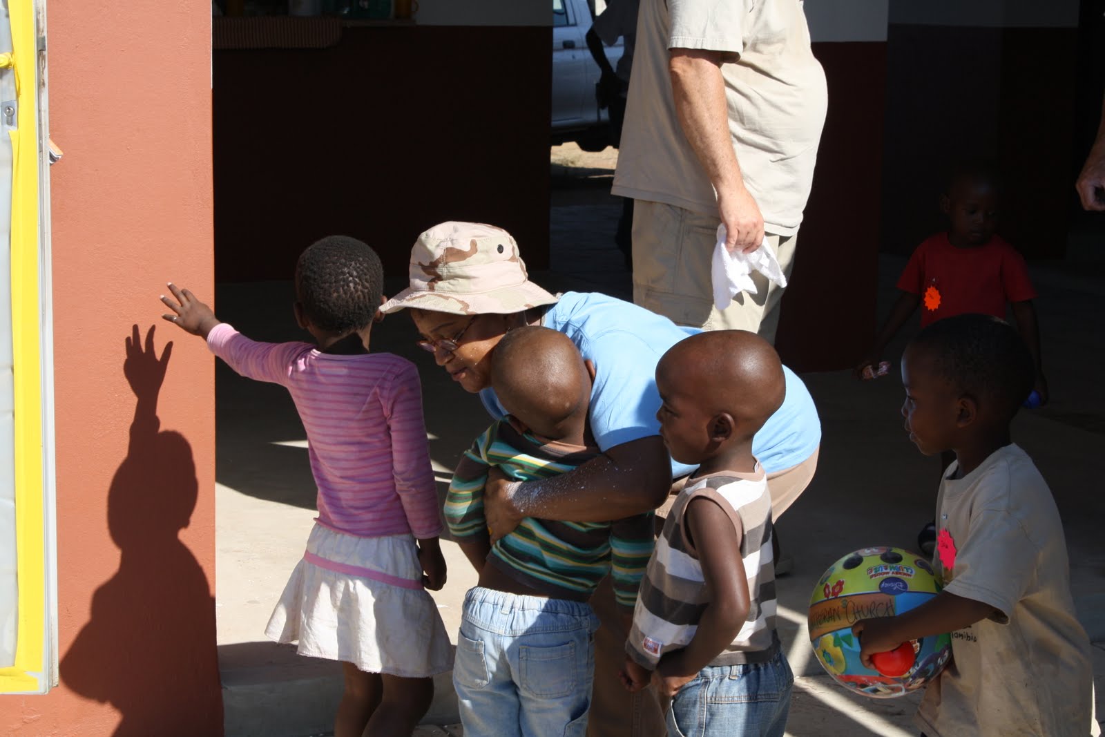 A Ntshongweni woman bending down to hug a small boy as other children gather around outside a community building