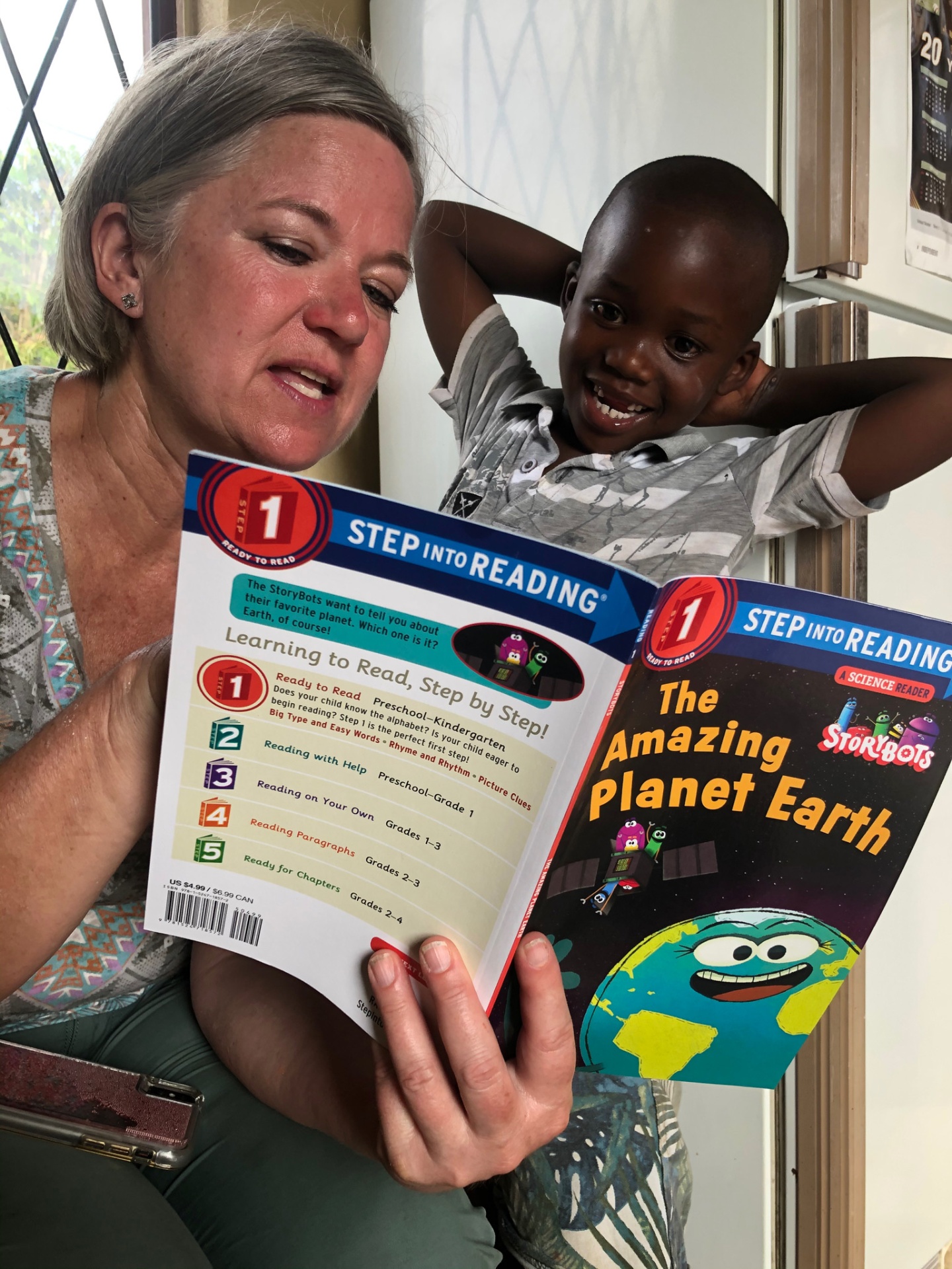 A friend of the mission reading a book aloud beside a smiling boy
