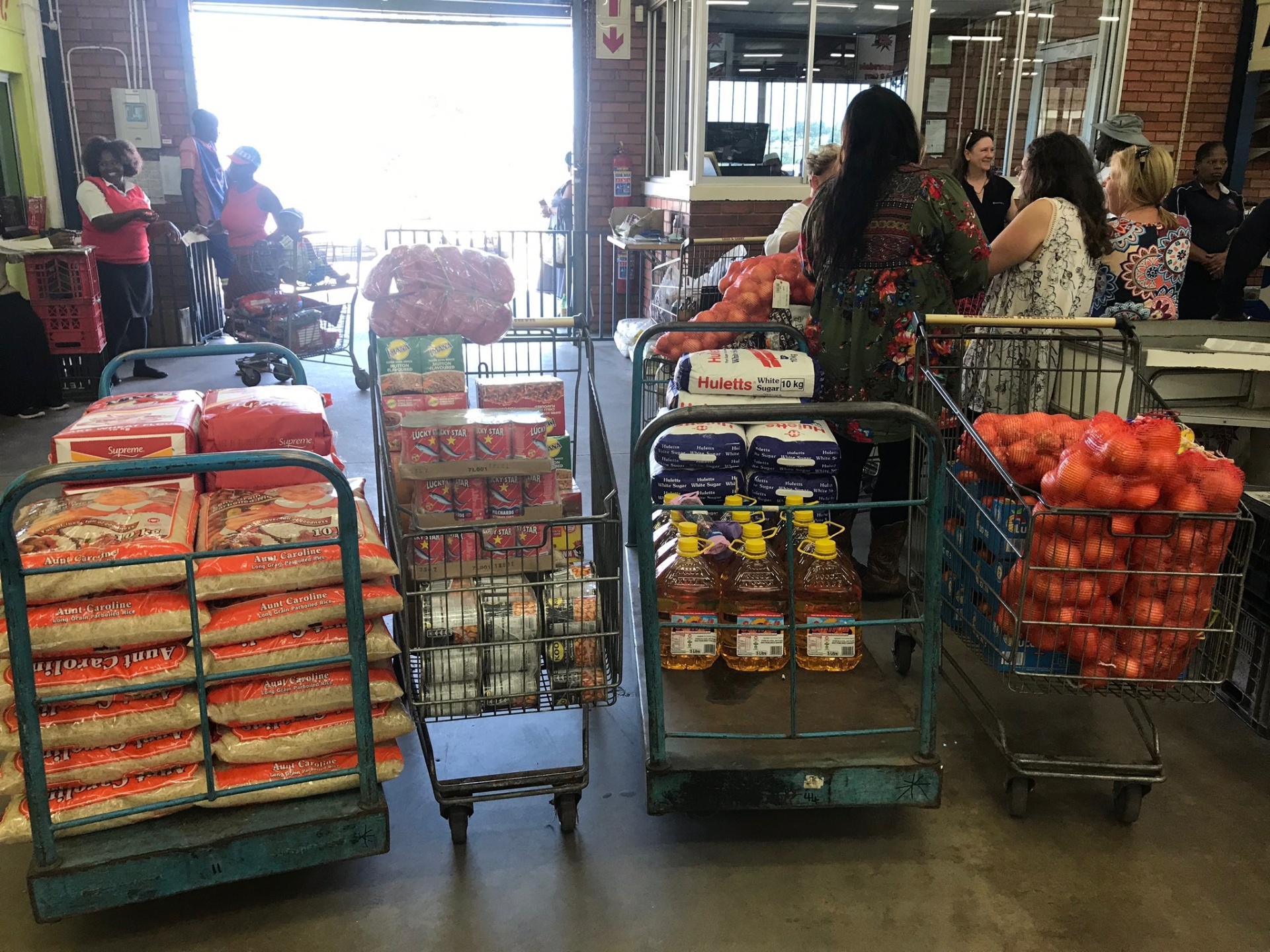 Flatbed carts loaded with rice, cooking oil, onions, sugar, and pantry staples lined up at the wholesaler before delivery day