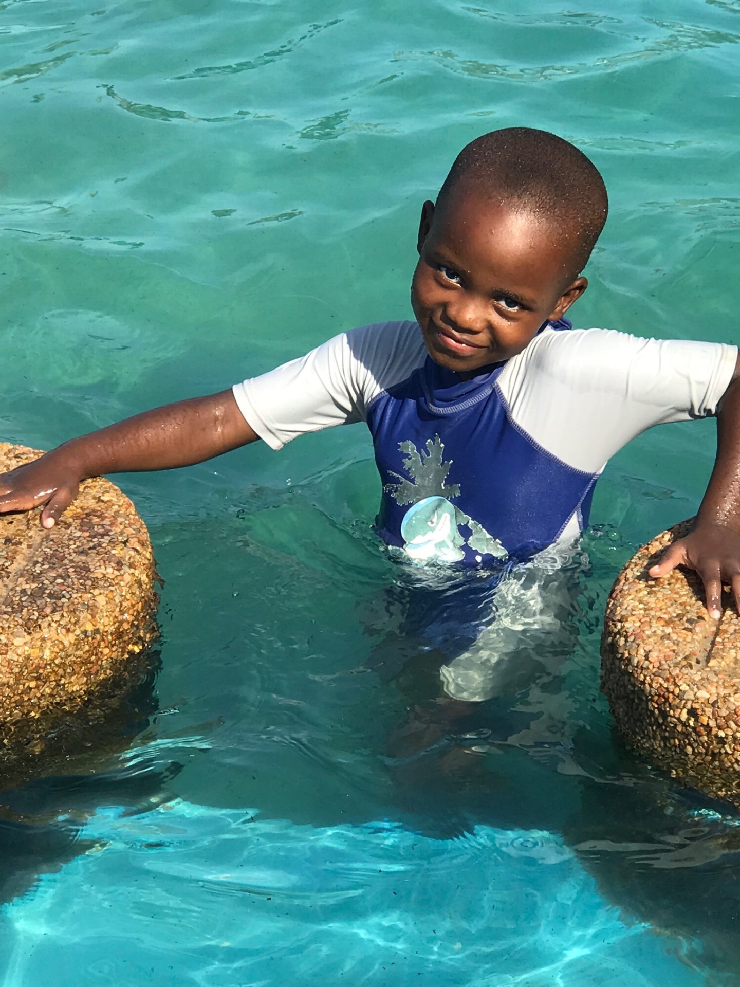 A delighted boy standing in the bright turquoise pool