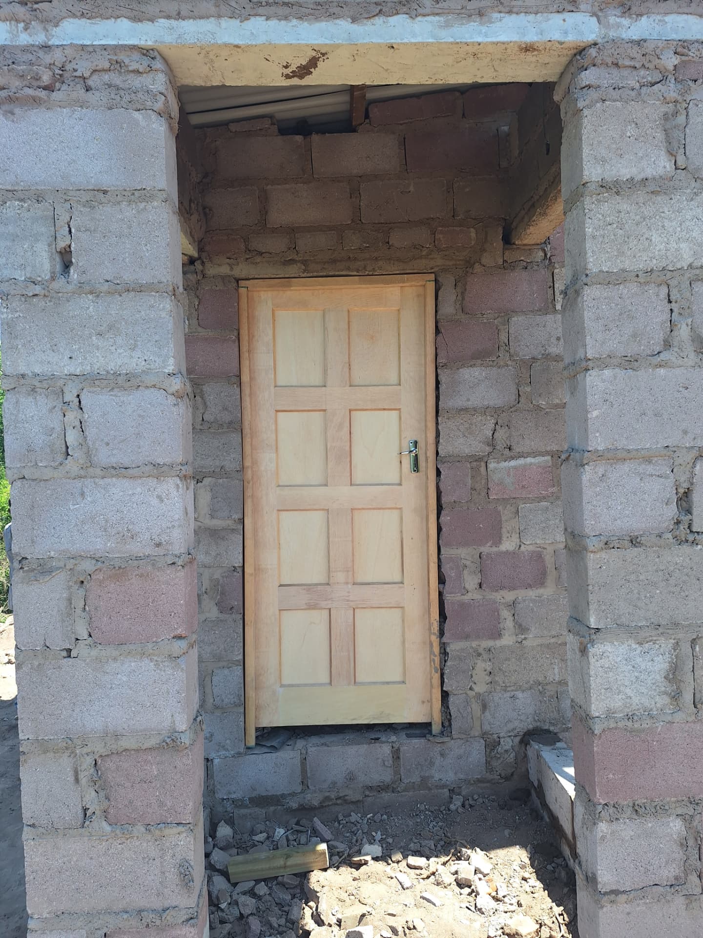 A second new wooden door framed by the unfinished block walls at the side of the house