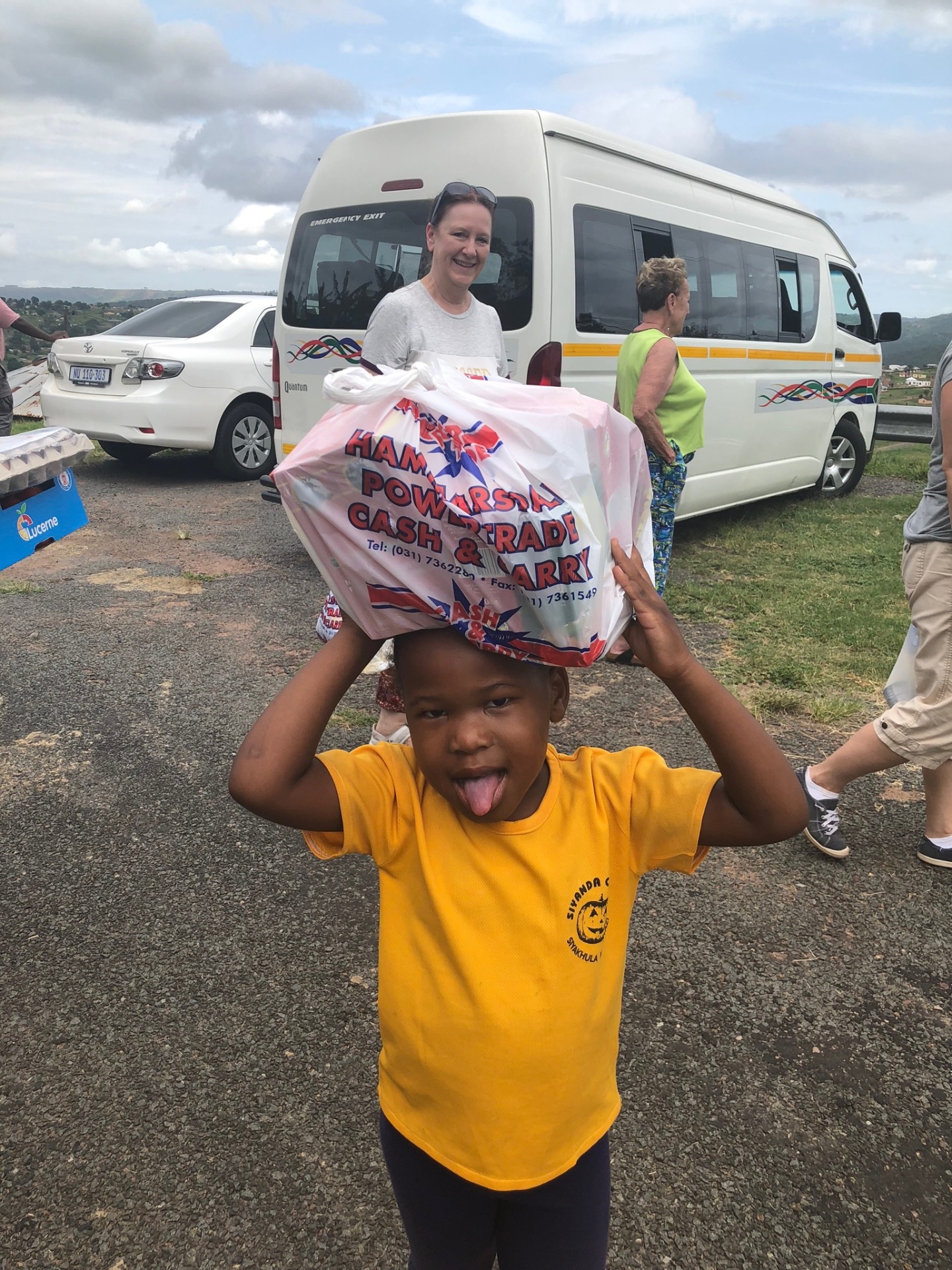 A grinning Ntshongweni boy balancing a full bag of food on his head, proud to help carry his family's parcel