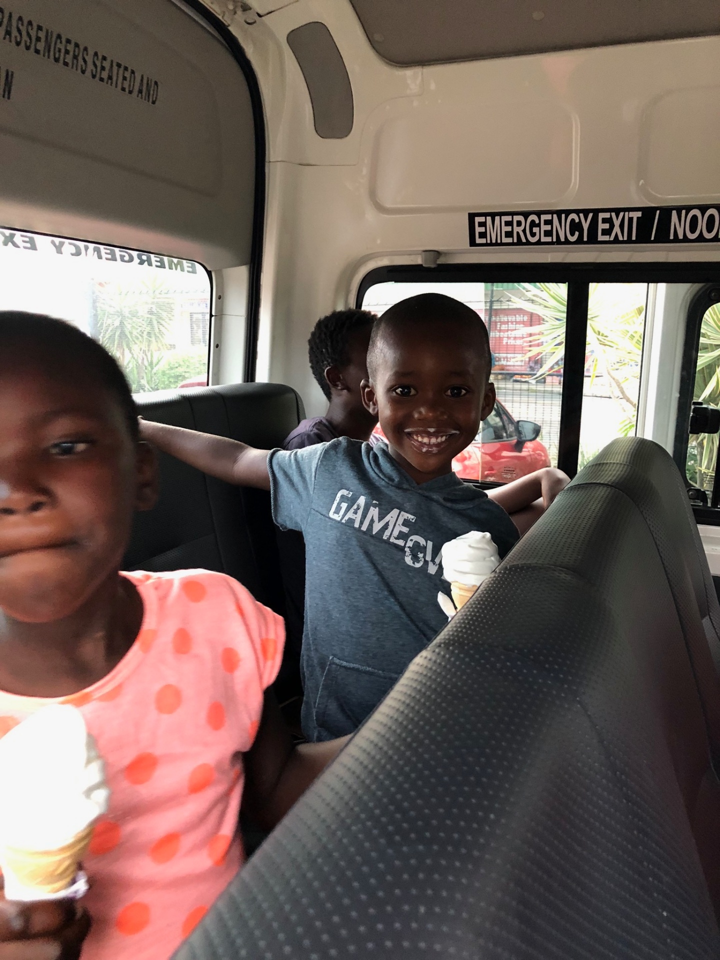 Two children grinning with soft-serve cones in the team van