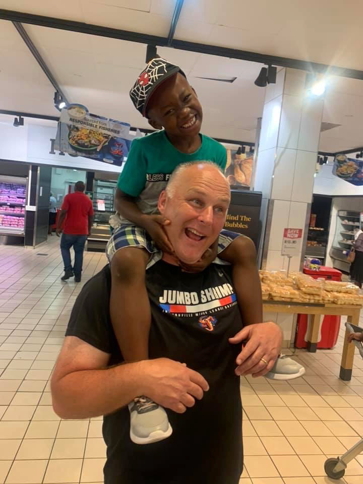 A laughing young boy sitting on a friend's shoulders in a shop aisle during an outing